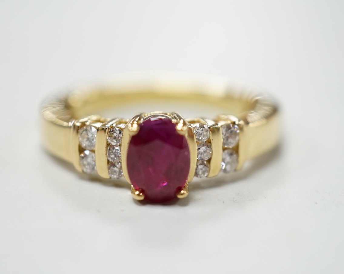 A modern yellow metal and single stone oval cut ruby set dress ring, with ten stone diamond chip set shoulders, size M, gross weight 5.7 grams.